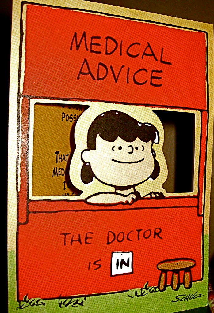 Lucy from the Peanuts cartoons sits in a red cardboard sidewalk stand that is labeled: “Medical advice: The doctor is IN”